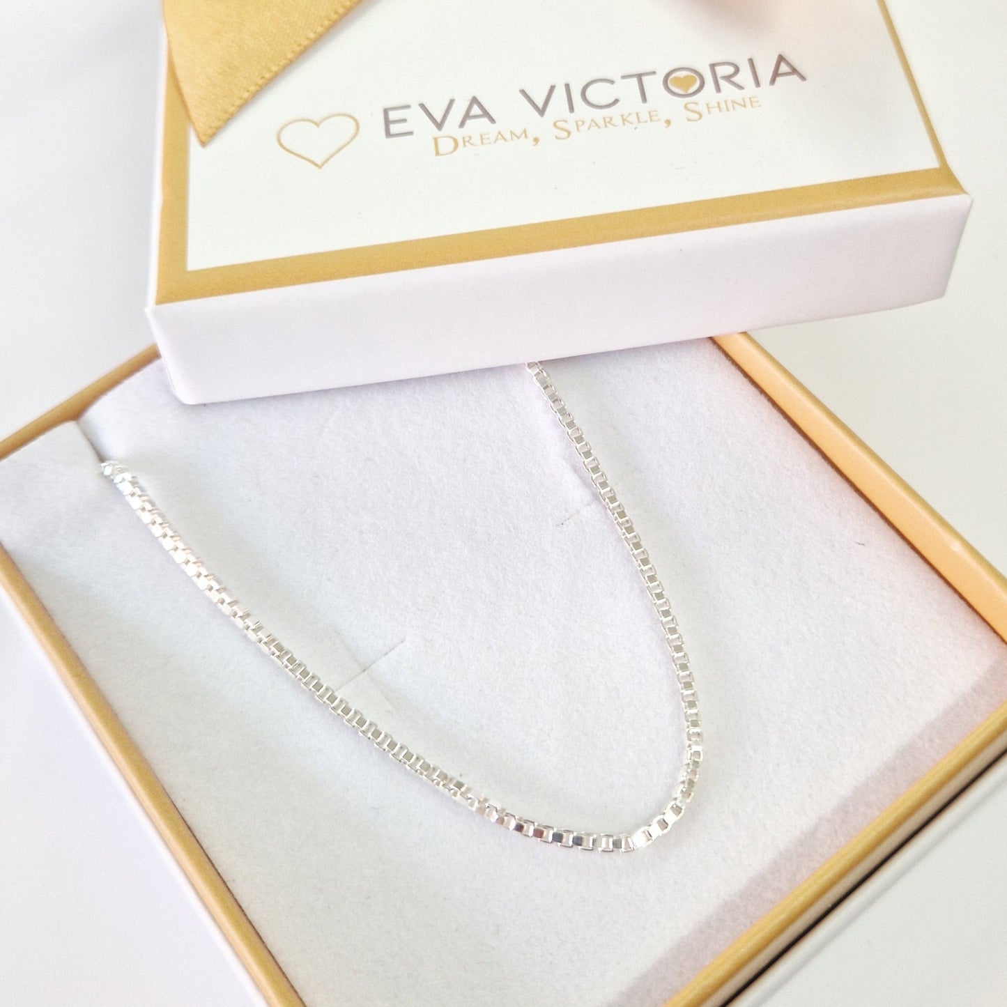 Jewelry box with a gold bow and 'Eva Victoria' branding, containing asilver box link chain necklace.