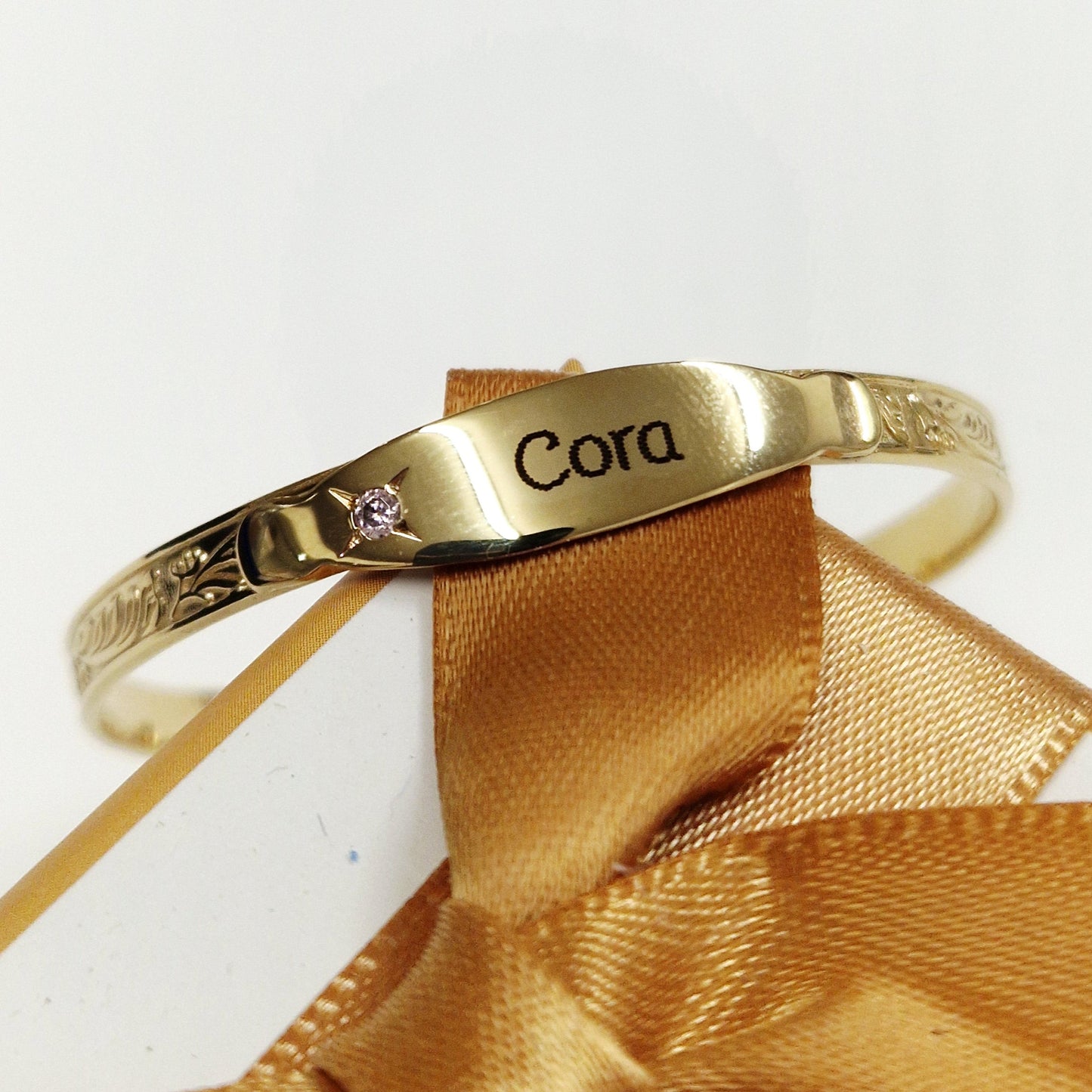 Gold baby bangle with laser engraving on a white background