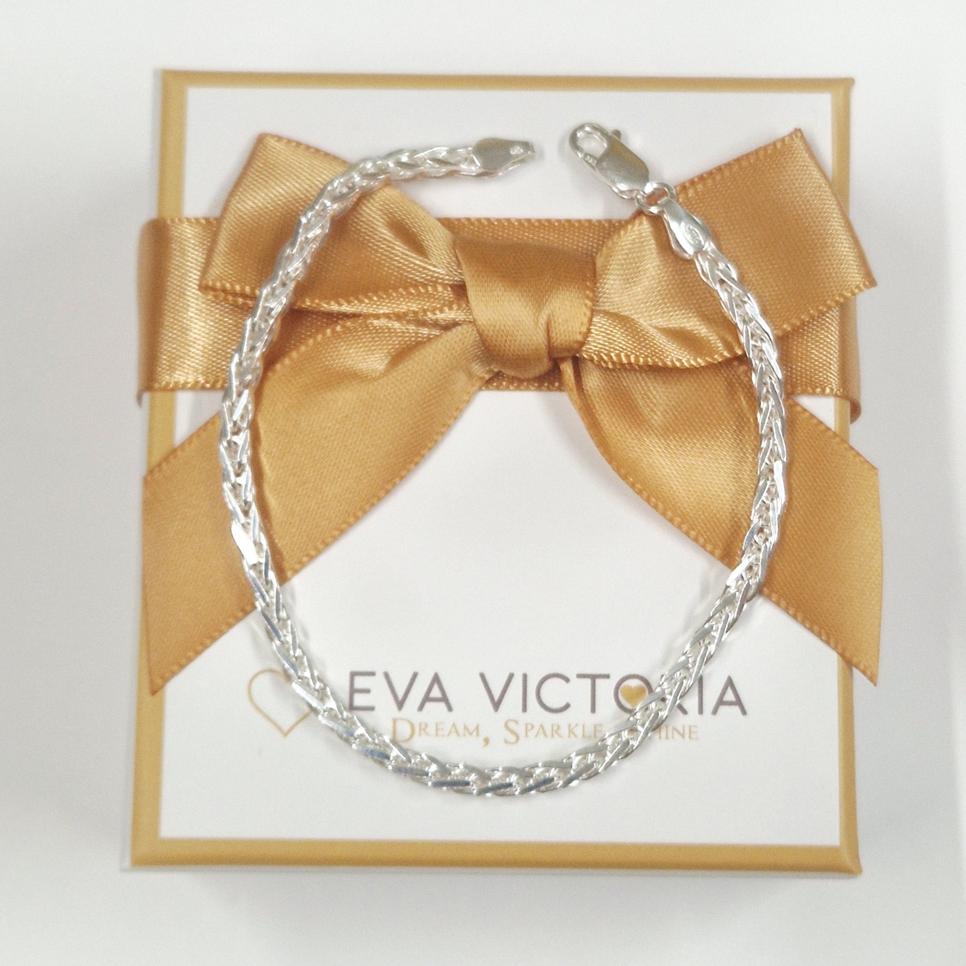 Silver spiga bracelet in a gold box with a bow on a white background