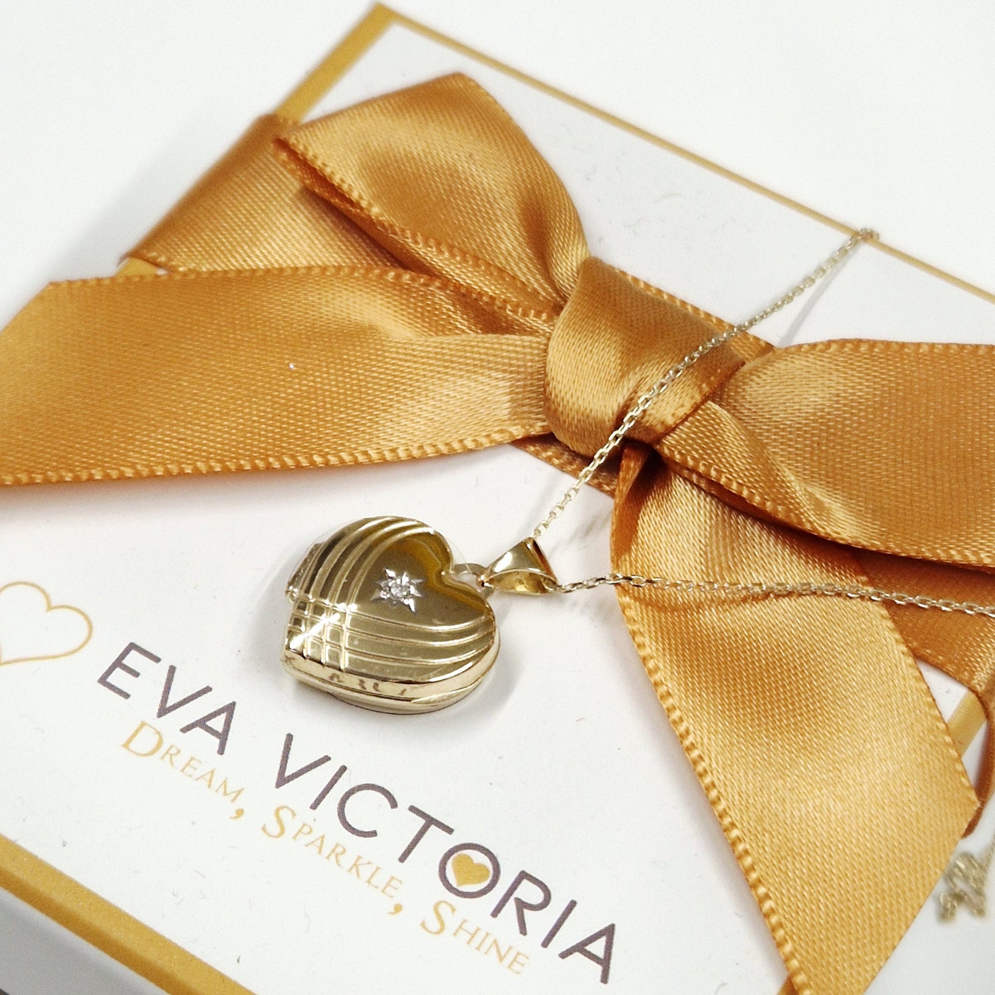 Gold necklace with heart pendant on a white card with gold ribbon, branded 'Eva Victoria'.