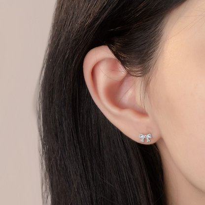 Close-up of an ear wearing a silver bow-shaped earring with a beige background