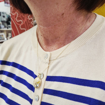 Close-up of a person wearing a white sweater with blue stripes, with a blurred indoor background.