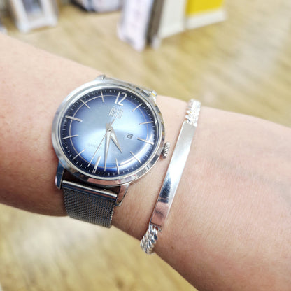 Silver watch with blue face on a wrist, blurred background